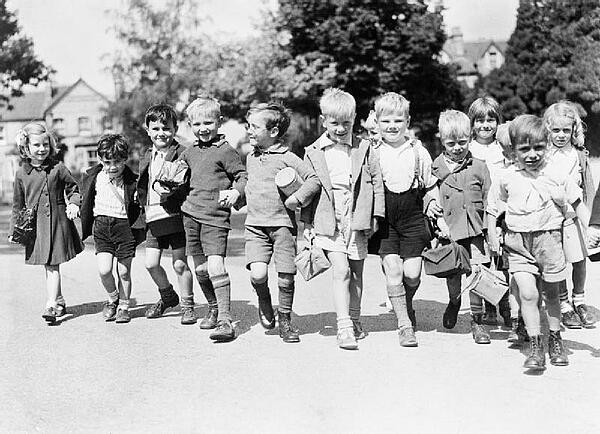 A group of smiling evacuees from Rotherhithe in Kent with gas mask boxes hold hands on a walk in Reading during 1940