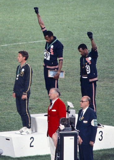 John Carlos(Right) & Tommie Smith(Center) showing the raised fist on the podium